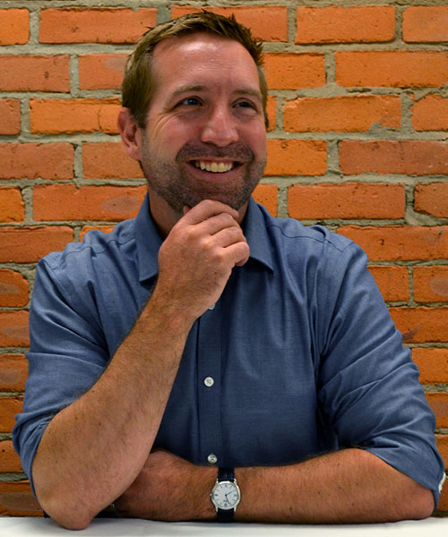 Staff headshot Doug Livingston, in front of a brick background.